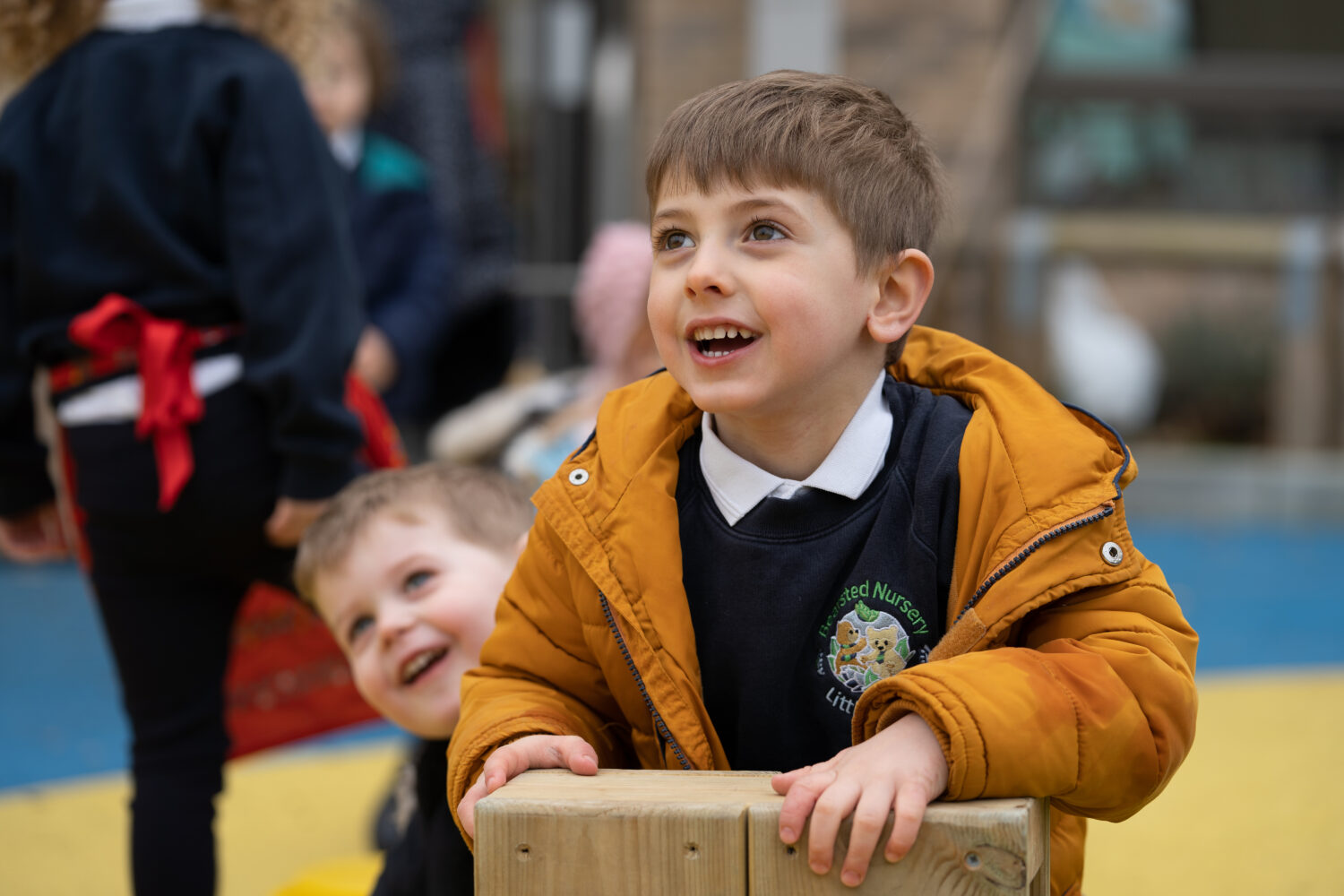 A young boy can be seen smiling brightly whilst wearing his winter coat in an outdoor area on the academy grounds.