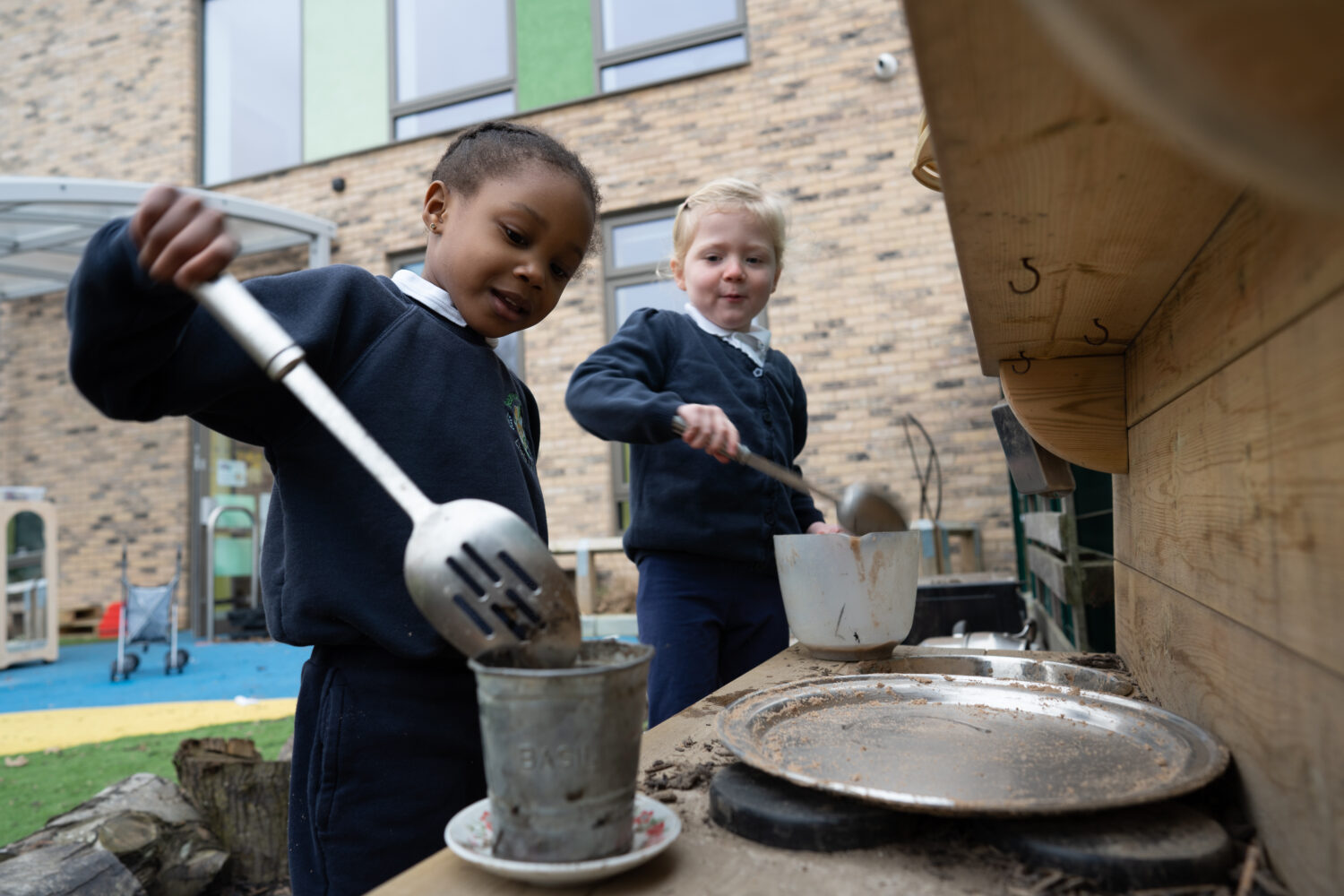 Two female pupils are pictured outdoors on the academy grounds, using cooking utensils to stir cake mixture in a large bowl.